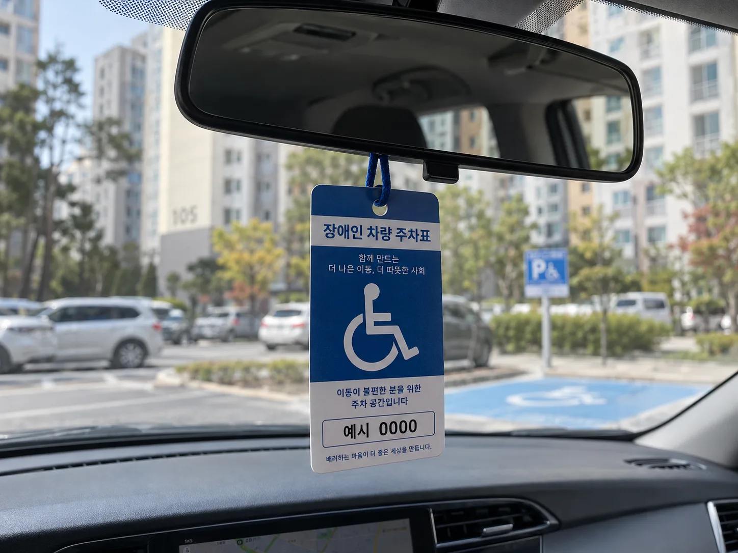 자동차 실내에서 백미러에 걸린 장애인 차량 주차표지, 창밖으로 장애인전용주차구역이 보이는 모습