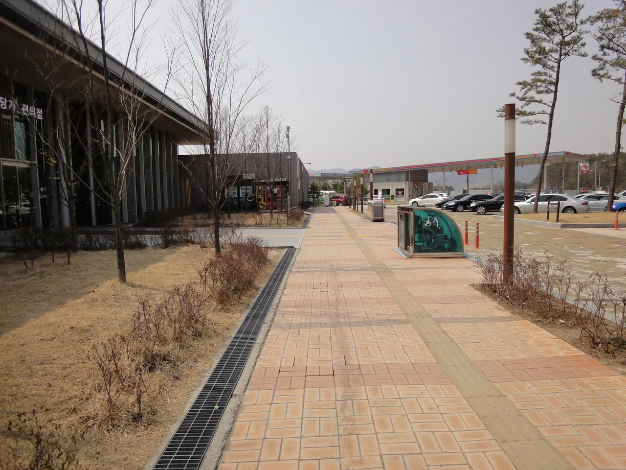 고속도로 휴게소 주차장과 편의시설, 산책로가 이어진 전경, 승용차 여러 대가 주차돼 있는 모습