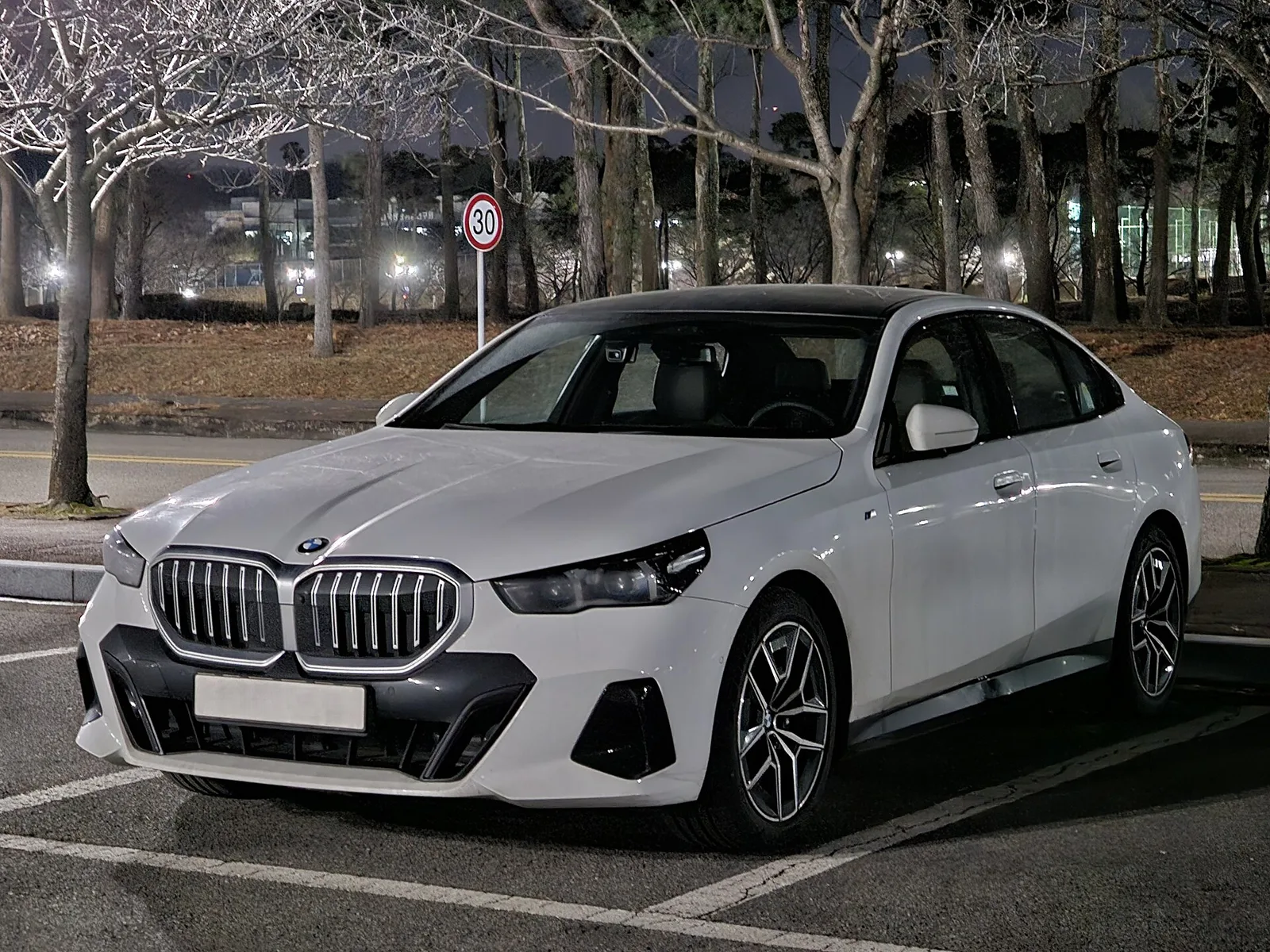 야간 주차장에 세워 둔 흰색 BMW 5시리즈(G60) 세단의 전면 3/4 모습