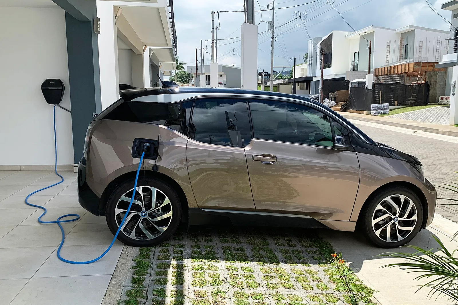주택 앞에 주차된 BMW i3가 벽면 충전기에 케이블로 연결돼 충전 중인 모습