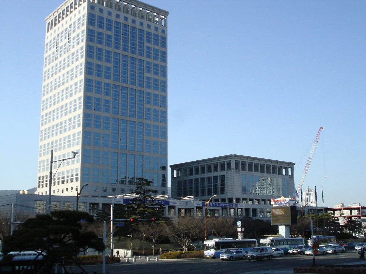 부산 시내 교차로 건너편에 서 있는 부산광역시청 고층 건물과 그 앞을 지나는 버스와 승용차들