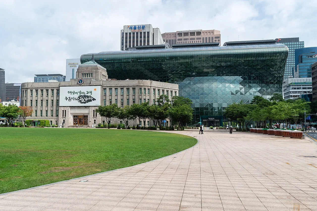 서울광장 잔디밭 너머로 보이는 서울특별시청 구청사와 유리 곡면으로 이루어진 신청사 건물 전경