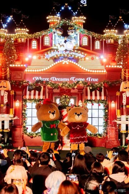 크리스마스 장식 건물 앞 무대에 곰 캐릭터 둘이 서 있고 관람객이 모인 모습