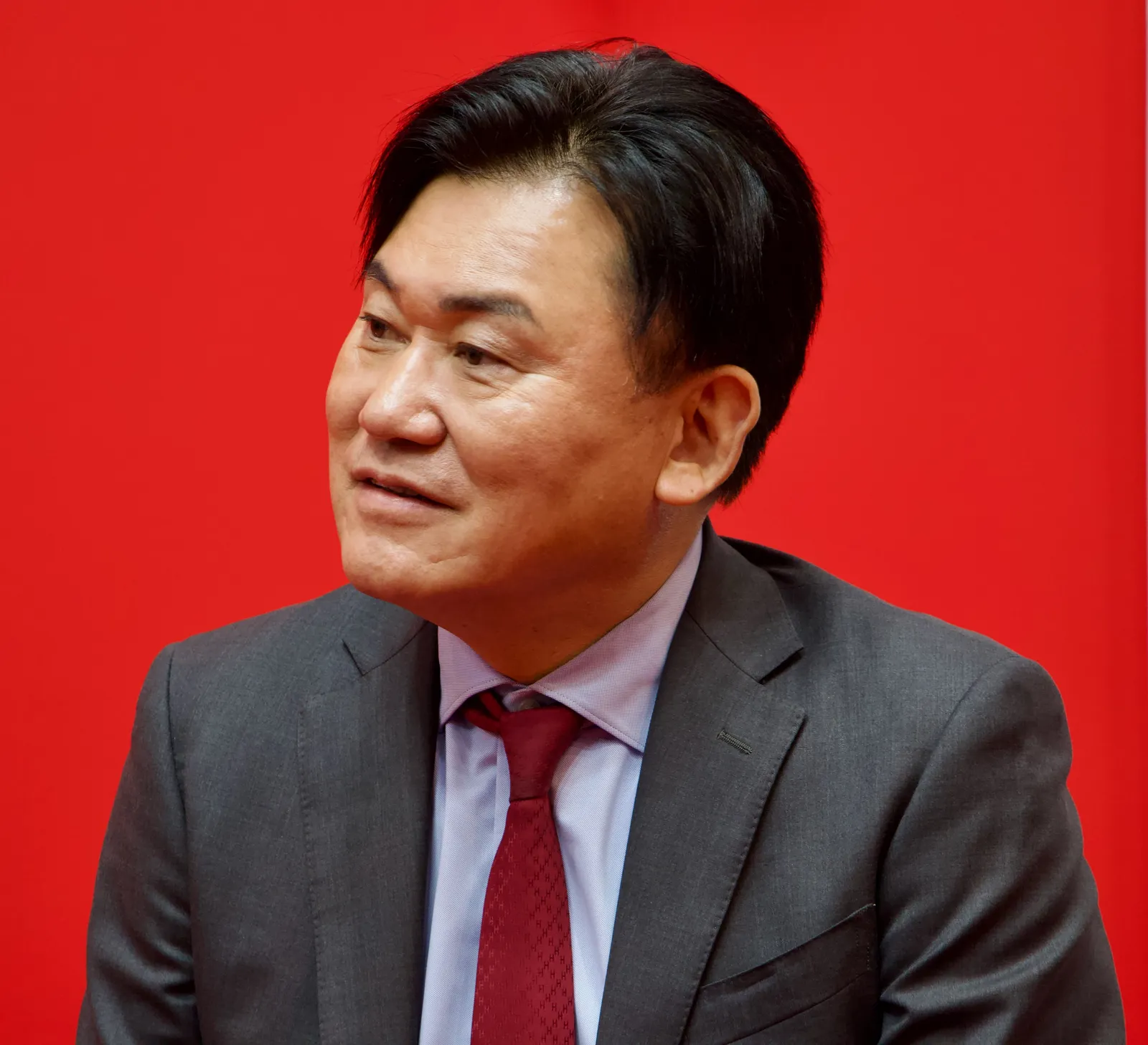 붉은 배경 앞에서 정장을 입고 인터뷰에 응하는 라쿠텐 미키타니 히로시 회장의 모습