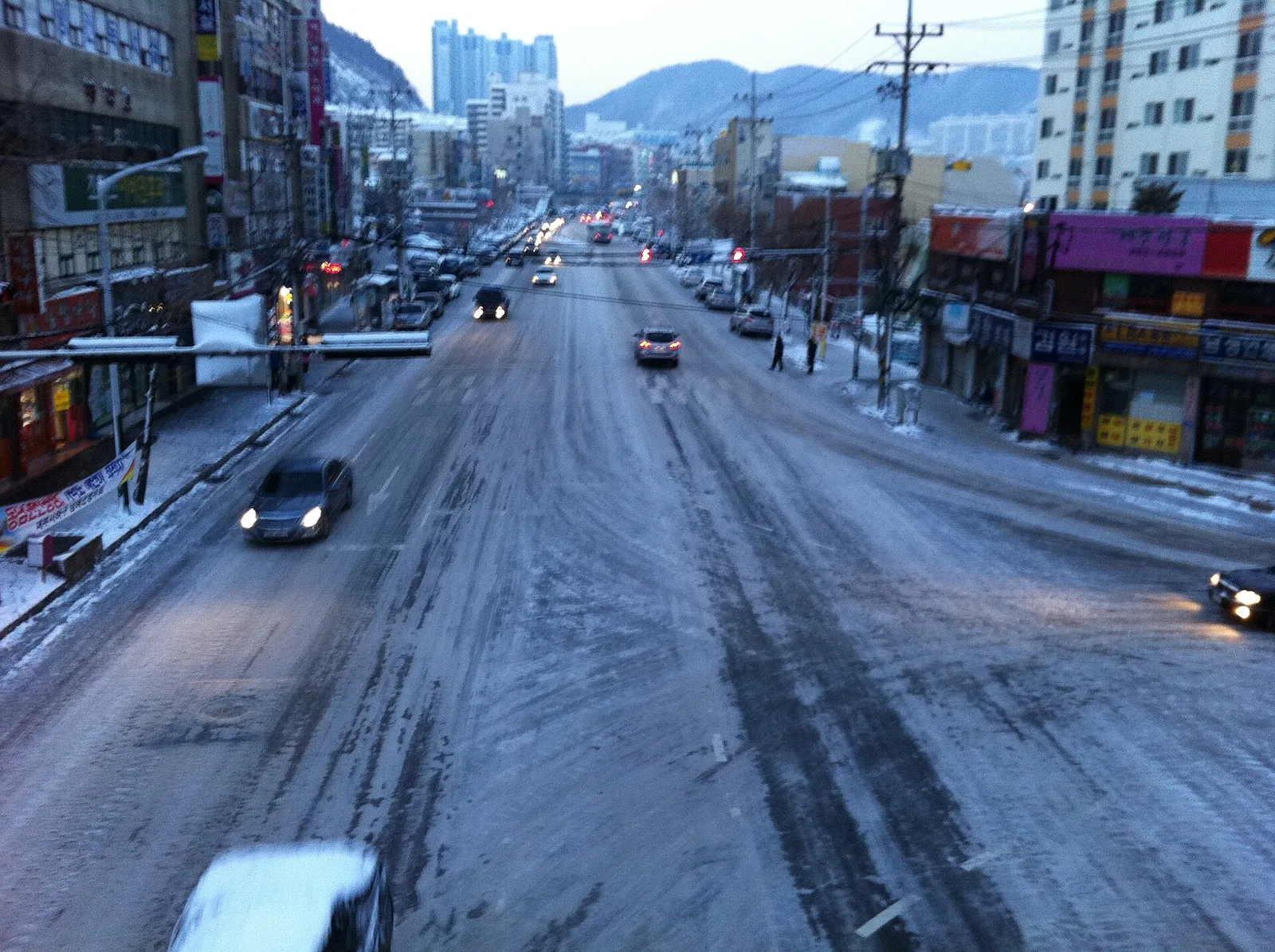 눈이 쌓인 부산 도심 도로에 차량 몇 대가 지나가는 저녁 풍경
