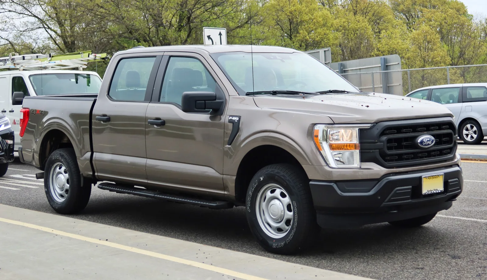 베이지색 포드 F-150 XL 슈퍼크루의 전면 및 측면 모습, 사다리꼴 그릴과 F-150 레터링이 보인다