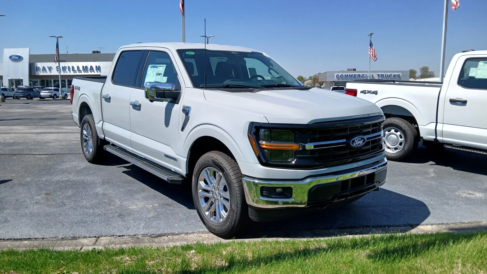 흰색 포드 F-150 XLT 슈퍼크루의 전면 및 측면 모습, 사다리꼴 그릴과 F-150 레터링이 보인다