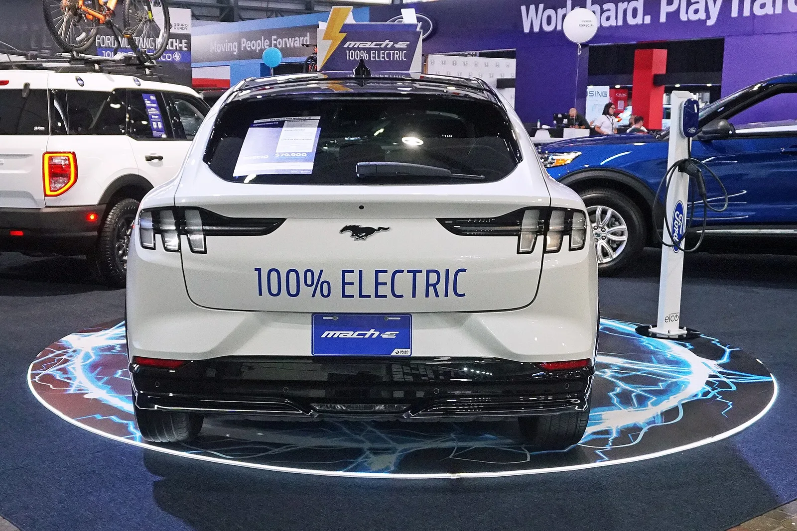 전시장에 놓인 흰색 포드 머스탱 마하-E 후면, 번호판 자리에 100% ELECTRIC 문구