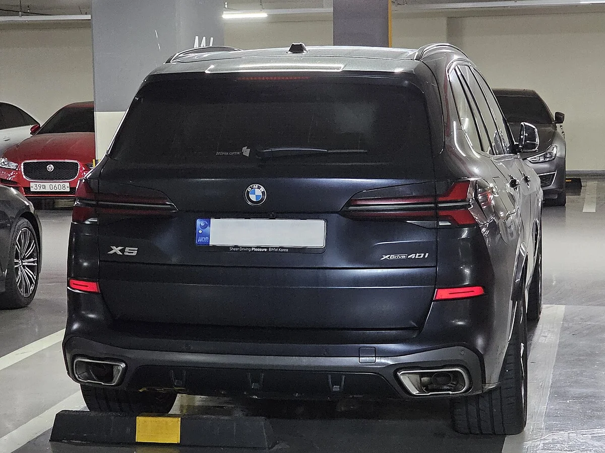 지하 주차장에 세워 둔 어두운 색 BMW X5 xDrive40i M 스포츠의 후면, 테일램프와 배기구가 보인다