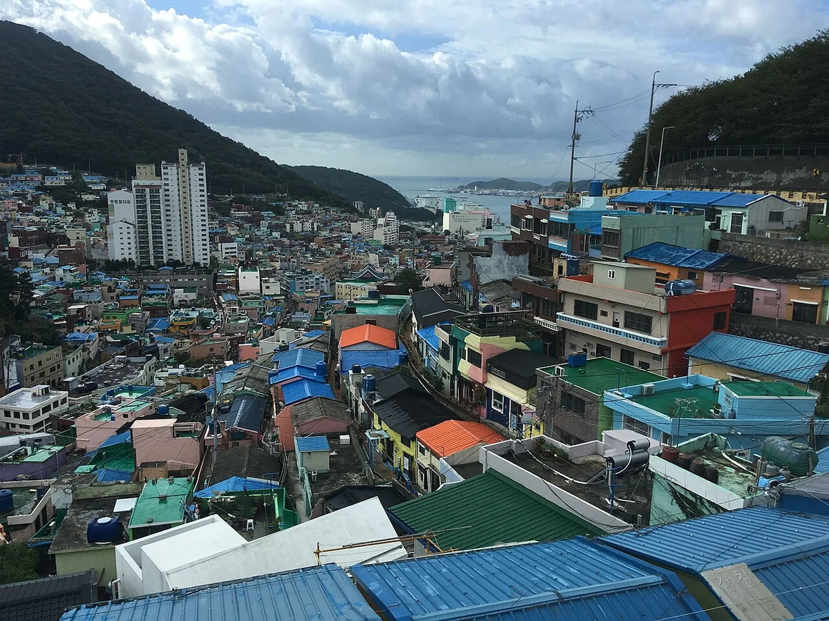 언덕을 따라 이어진 지붕들 너머 멀리 바다와 항구, 아파트가 보이는 감천문화마을 전경