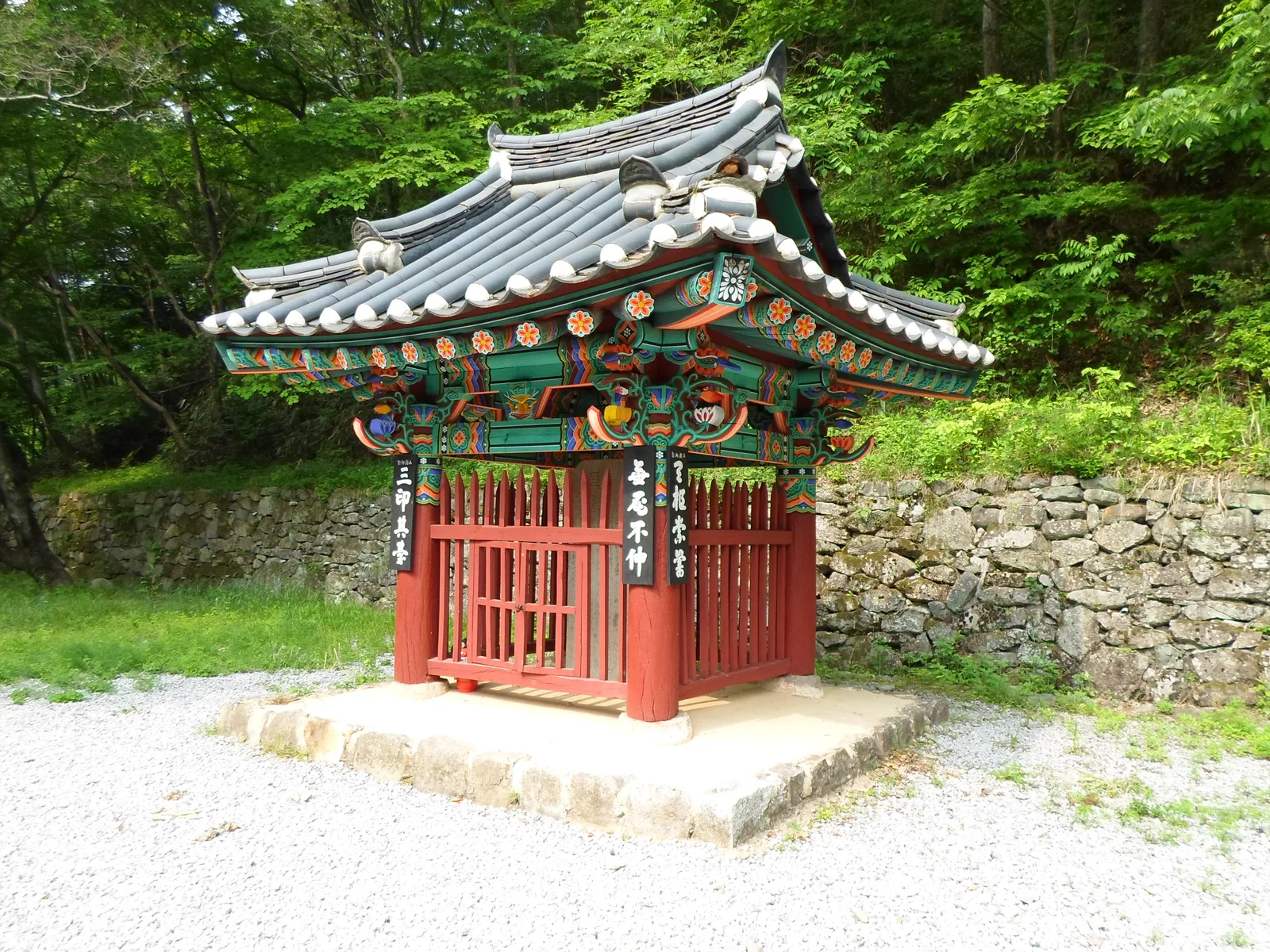 울창한 숲 속에 자리한 삼인대 비각, 단청이 화려한 지붕과 붉은 나무 울타리로 둘러싸여 있다