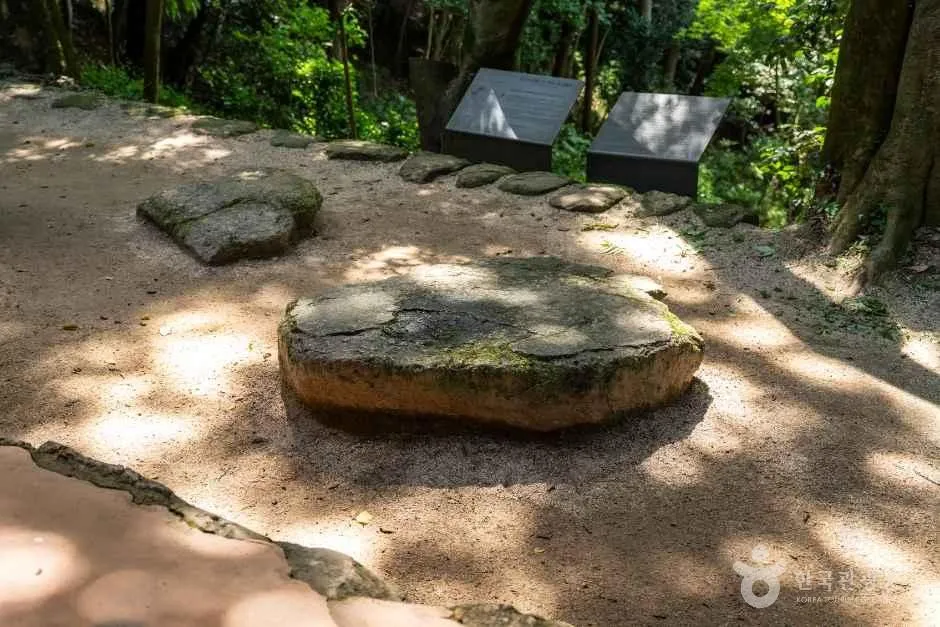 숲속 흙길 옆에 놓인 넓적한 돌과 안내판