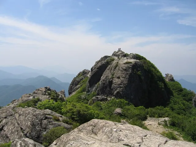 바위로 이루어진 가야산 상왕봉 정상에 등산객 몇 명이 서 있는 모습, 뒤로 겹겹이 이어진 산줄기