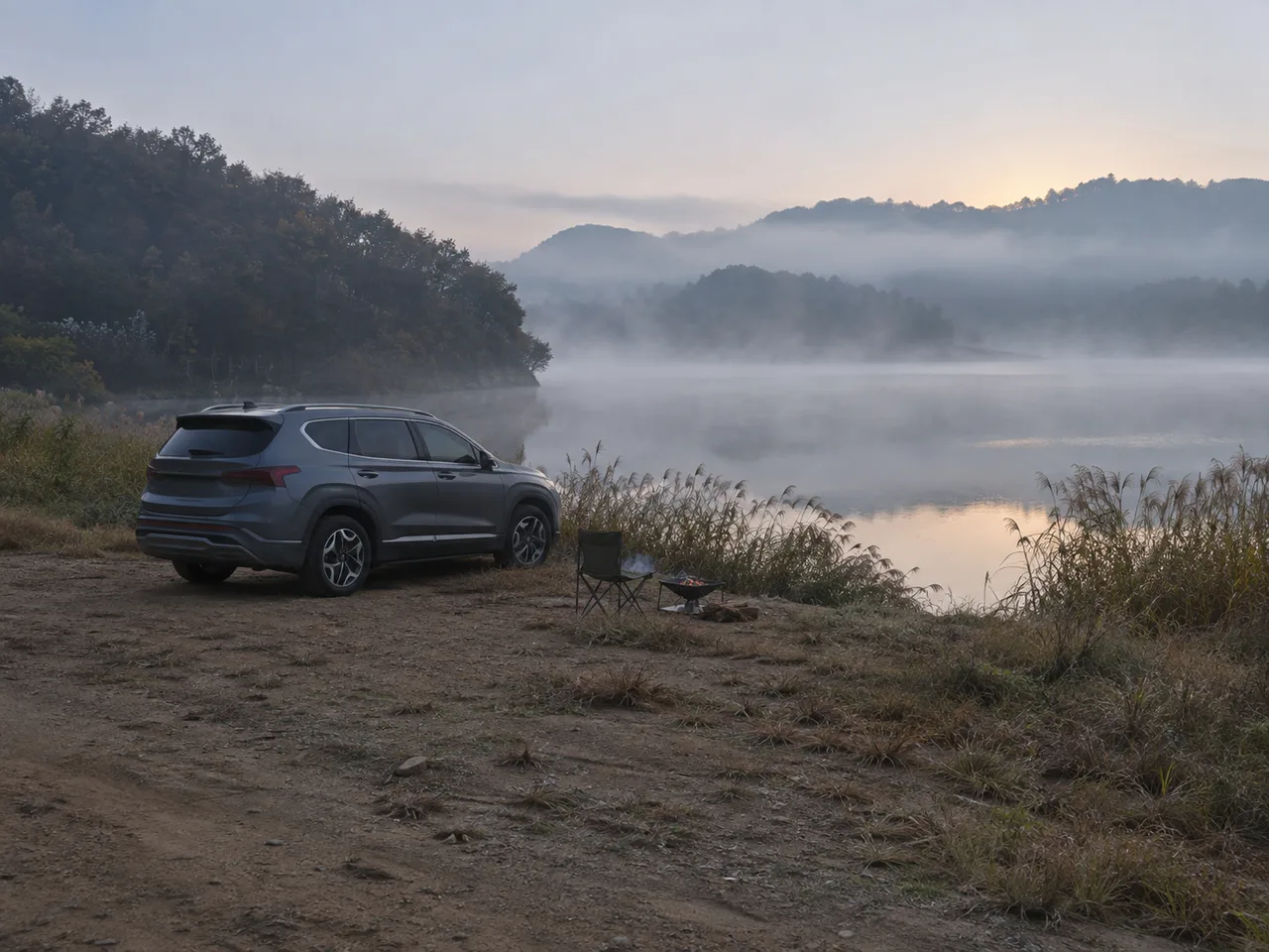 물안개가 낀 저수지 노지 차박지에 SUV 한 대와 캠핑 의자, 화로대가 놓여 있는 이른 아침 풍경 연출 이미지