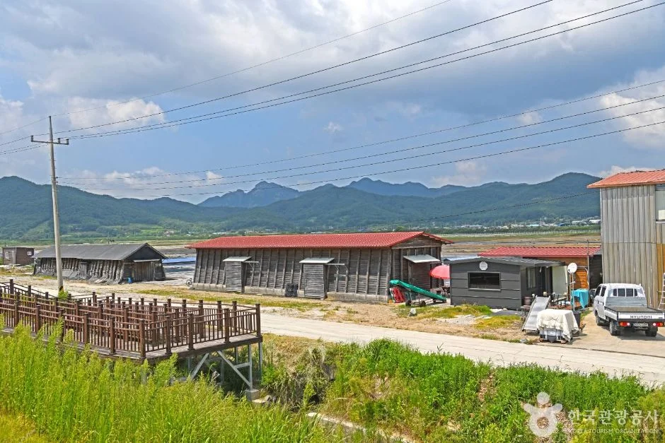 목재 데크 앞으로 염전 창고 건물과 산이 보이는 곰소염전 풍경