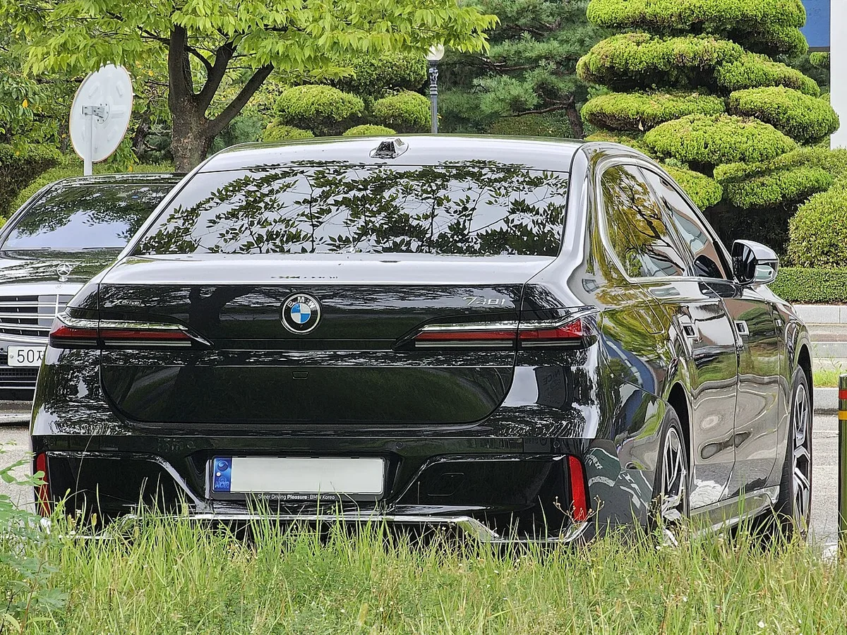 잔디와 나무 앞에 주차된 검은색 7세대 BMW 740i xDrive 세단의 후면