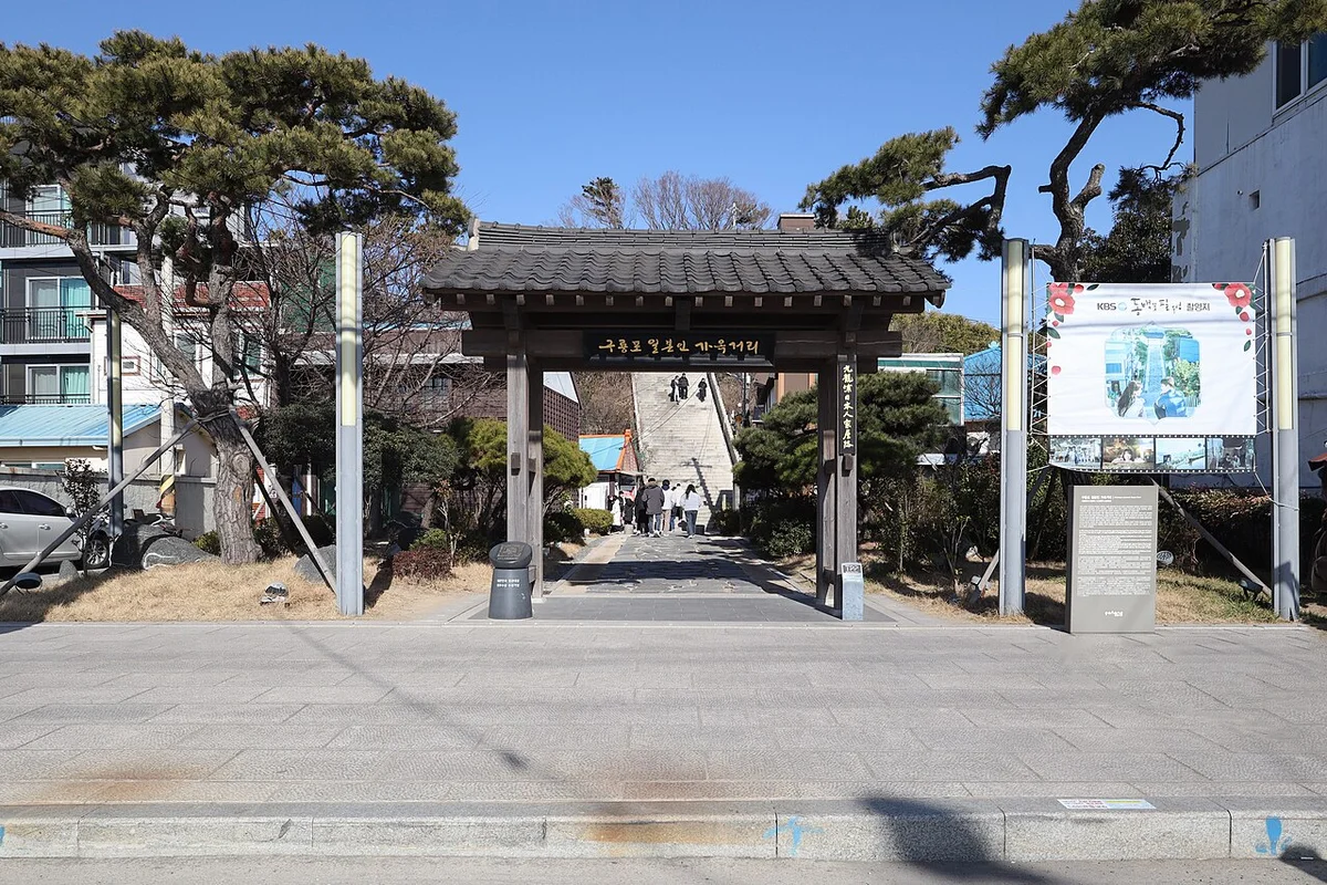 계단 위쪽에 기와지붕 문이 서 있고 앙상한 나무가 둘러선 구룡포공원 입구