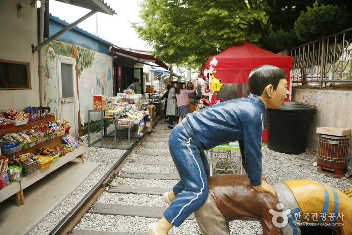 철길 옆에 서 있는 어린이 조형물과 양쪽으로 늘어선 가게들