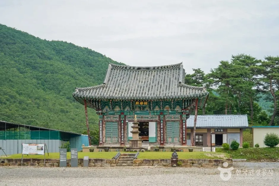 초록 산을 배경으로 선 단청 전각과 앞마당