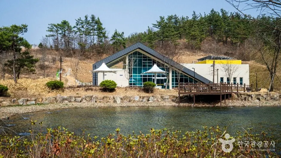 연못 뒤로 지붕이 보이는 건물과 억새