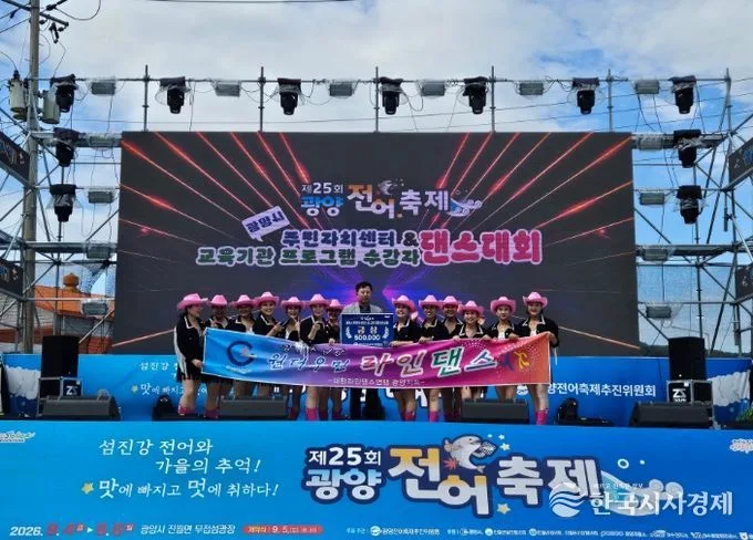 야외무대에서 카우걸 복장을 한 댄스팀이 주민자치센터 댄스대회 배너를 들고 공연하는 모습, 배경에 대형 LED 스크린이 있다