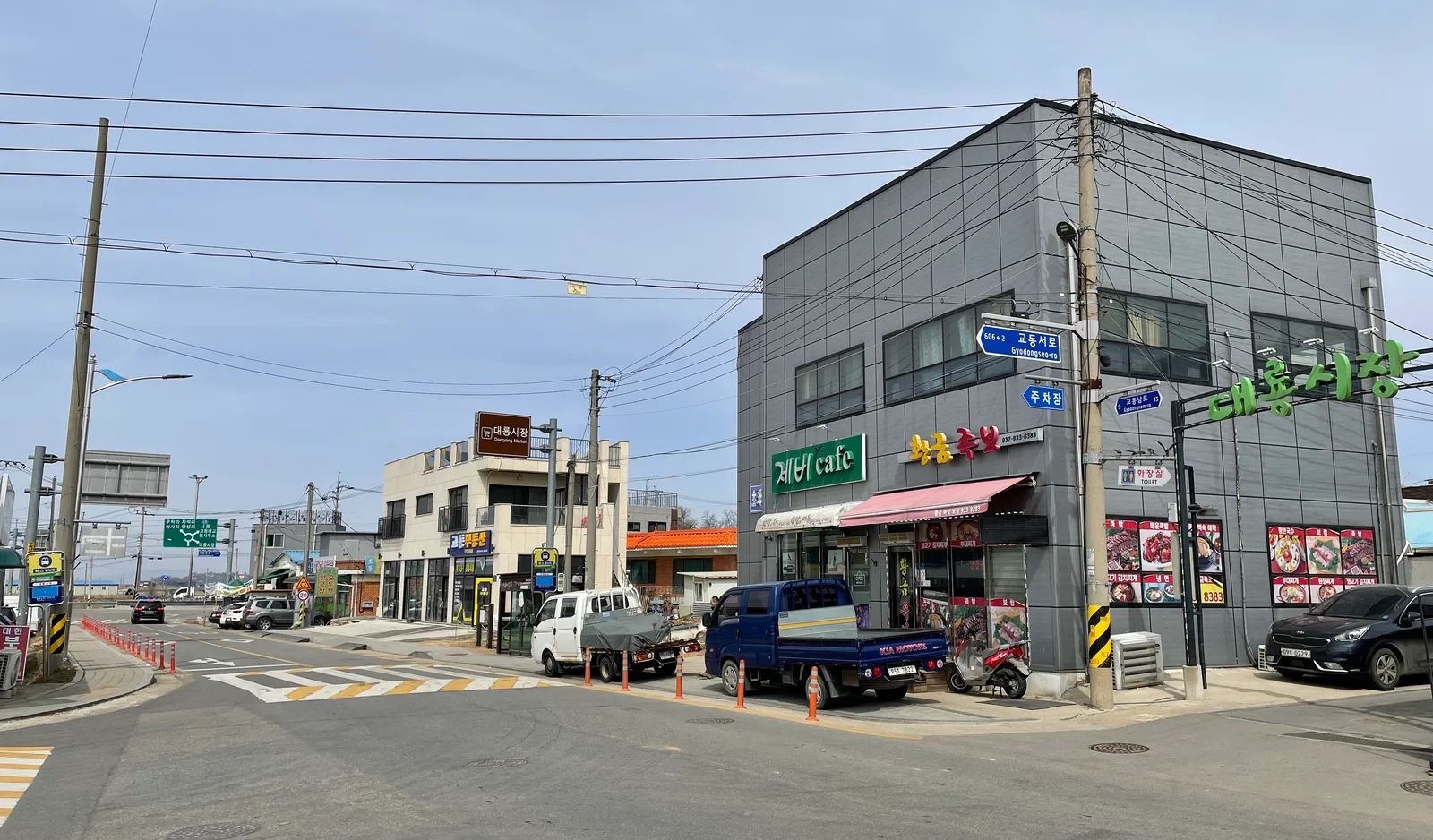 교차로 모퉁이 건물에 '대룡시장' 초록색 간판과 주차장 표지판이 걸려 있고 도로변에 트럭들이 서 있다