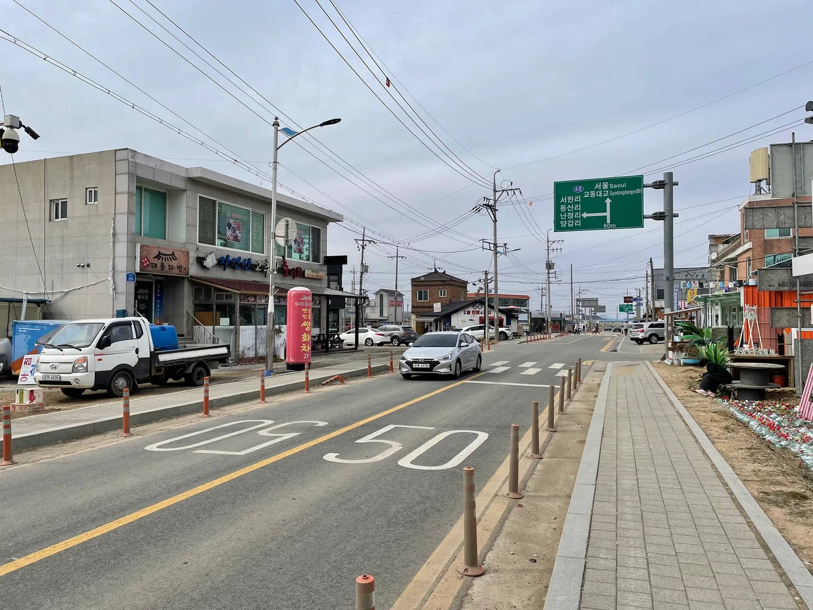 교동면 시가지 도로 위로 서울·교동대교 방향을 알리는 초록색 표지판이 걸려 있고 소형 승용차가 지나가는 모습