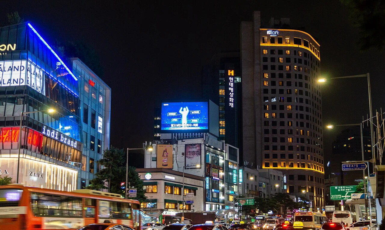 밤에 간판과 조명이 켜진 서울 도심 도로, 버스와 차량이 오가는 야경
