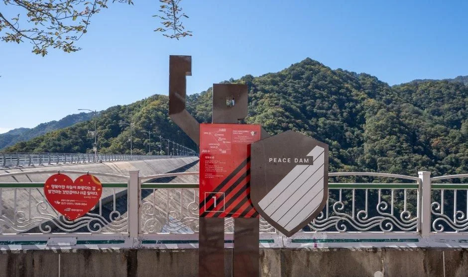산을 배경으로 한 PEACE DAM 안내 조형물과 난간