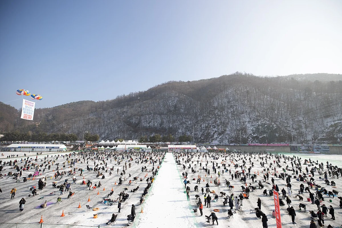 눈 쌓인 산을 배경으로 얼음판 위에 수많은 사람이 모인 산천어축제 현장