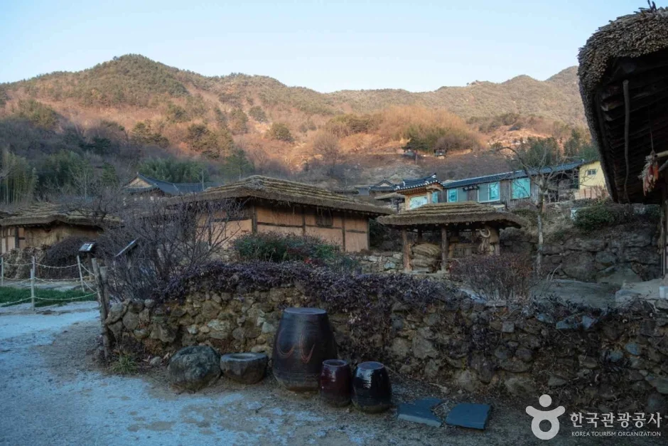 마른 풀빛 산 아래 돌담과 장독, 초가지붕 집들이 있는 마을