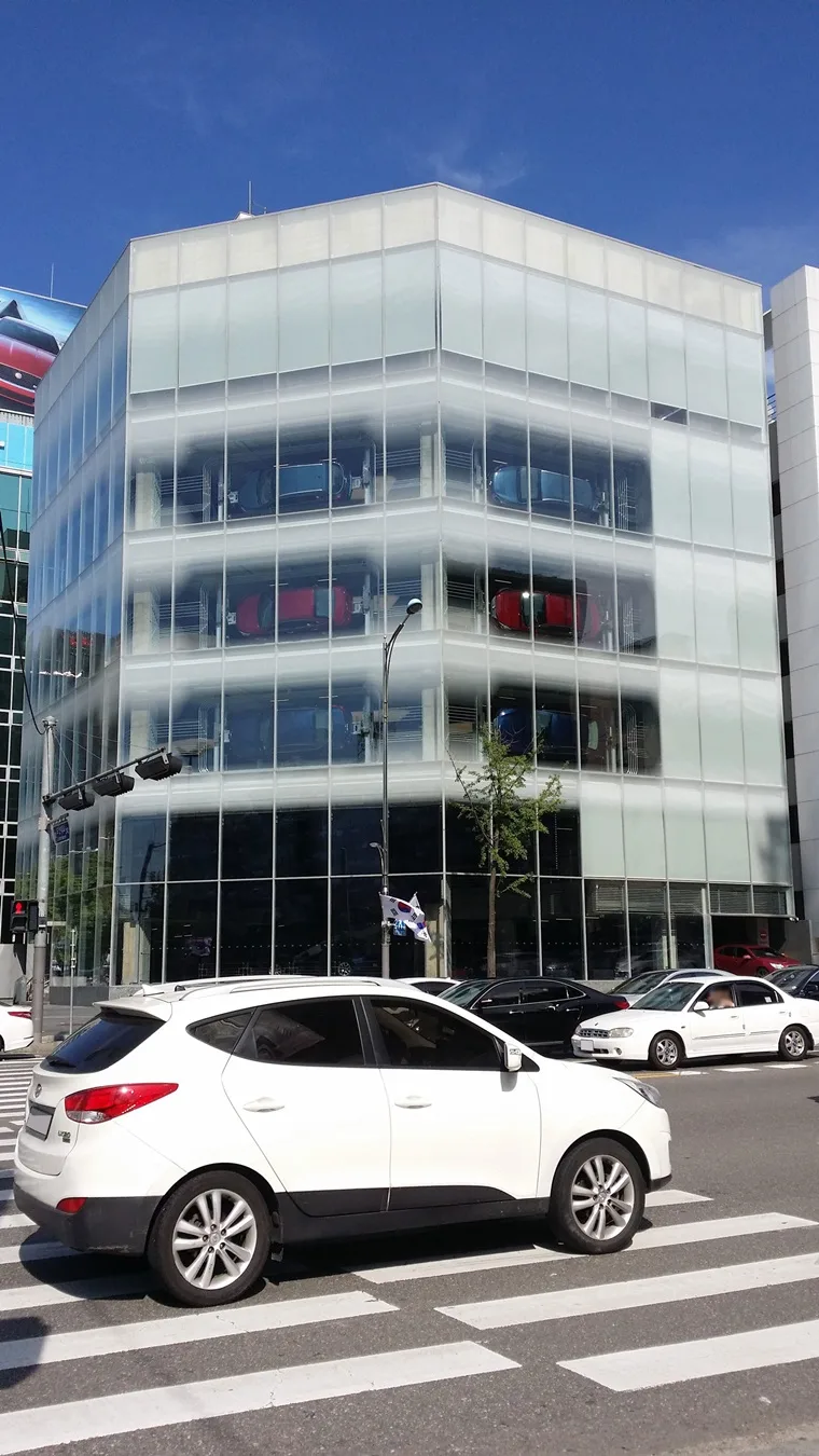 서울 도산대로변의 현대 모터스튜디오 서울 건물, 반투명 유리 외벽 너머로 층층이 걸린 차량이 비친다