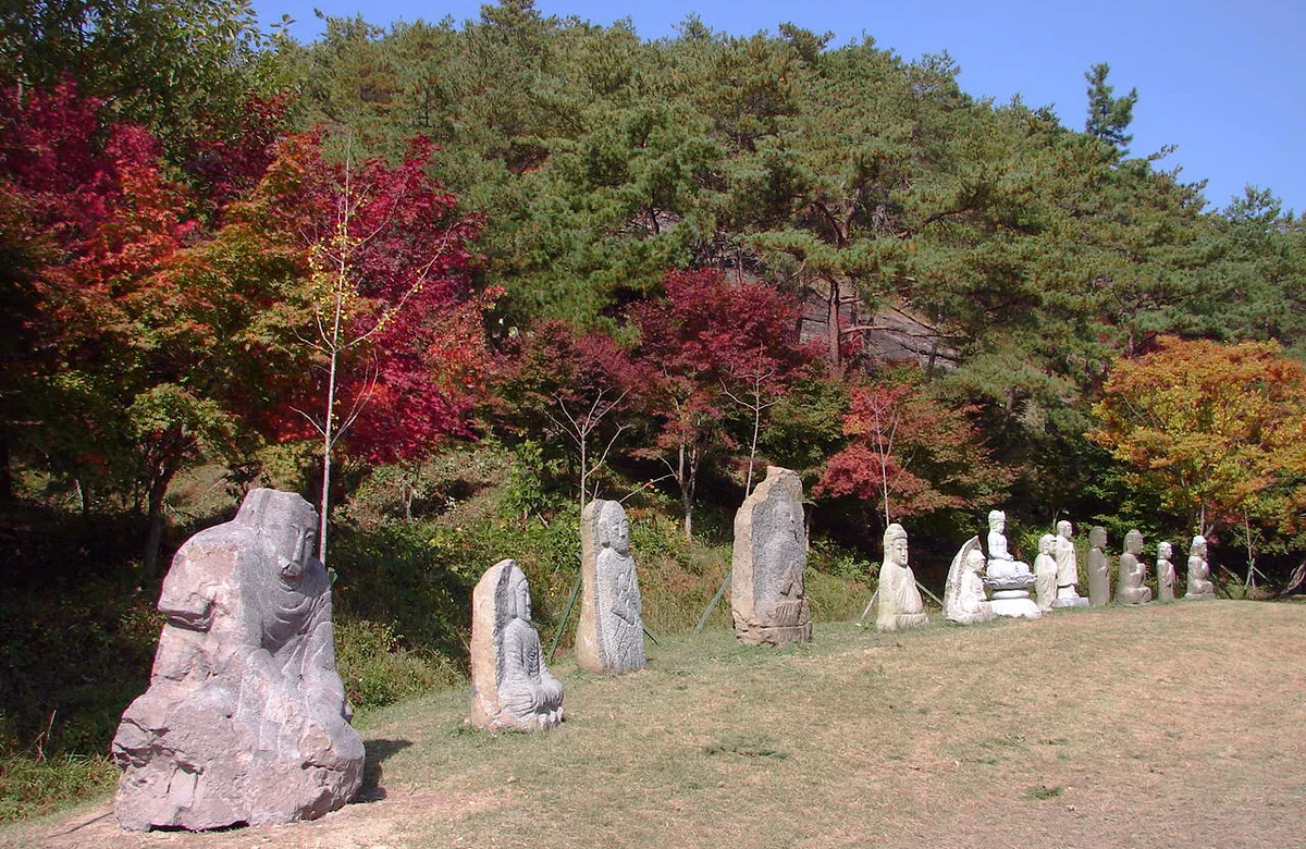 붉은 단풍나무와 소나무 아래 돌부처와 돌기둥이 줄지어 선 풀밭 길