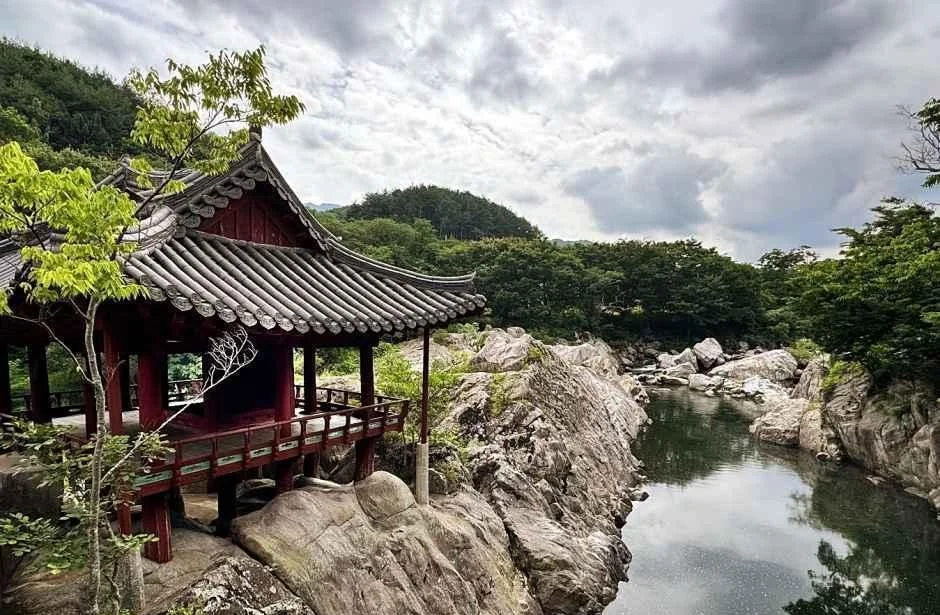 흐린 하늘 아래 바위 위에 자리한 거연정과 계곡물