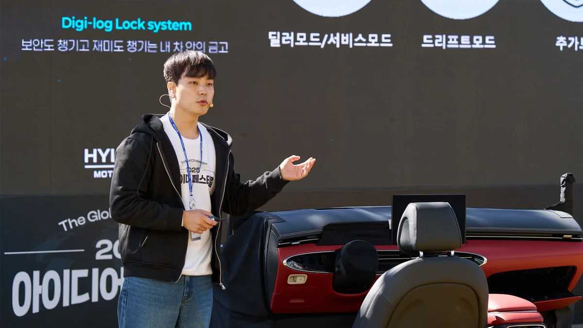 무대에서 빨간 차량 좌석 앞에 선 발표자가 잠금 시스템 시제품을 설명하는 모습