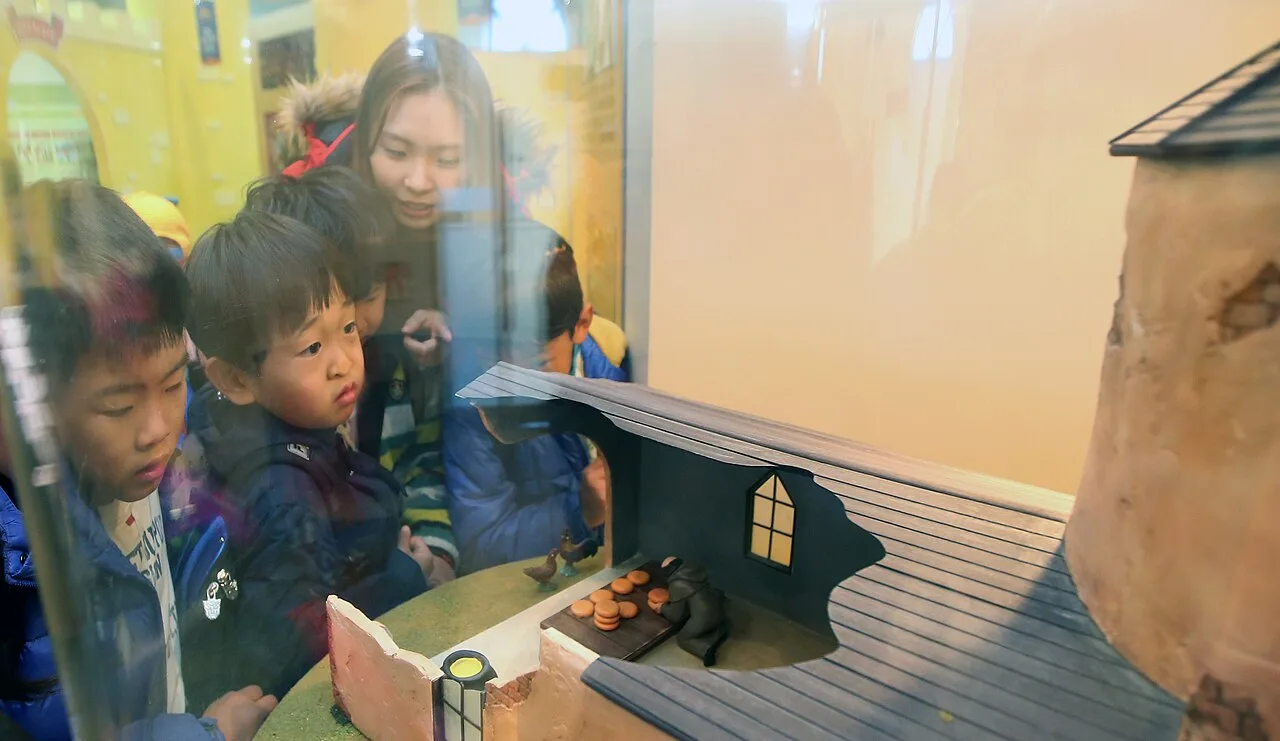 유리 전시창 너머로 옛 마을과 치즈 만드는 모습을 재현한 디오라마 모형을 아이들과 보호자가 들여다보는 모습