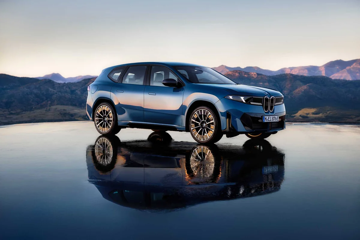 수면 위에 서 있는 파란색 BMW iX3의 전측면, 산을 배경으로 키드니 그릴과 반사된 차체가 보인다