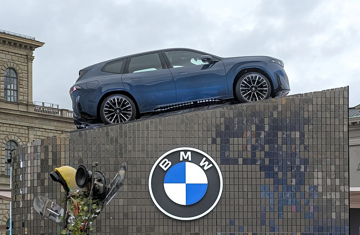 뮌헨 거리 전시대 위에 올려진 파란색 BMW iX3의 측면, 아래에 BMW 로고가 보인다