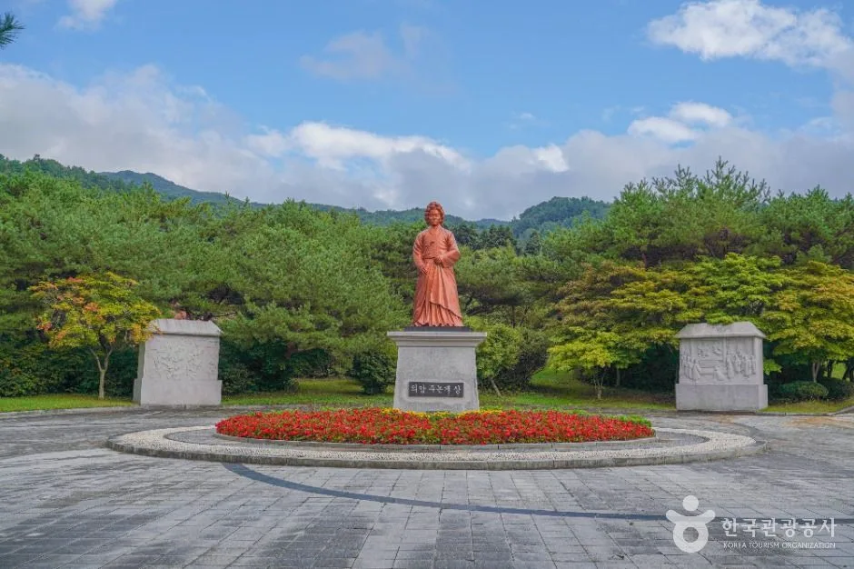 꽃밭으로 둘러싸인 원형 터 한가운데 서 있는 인물 동상