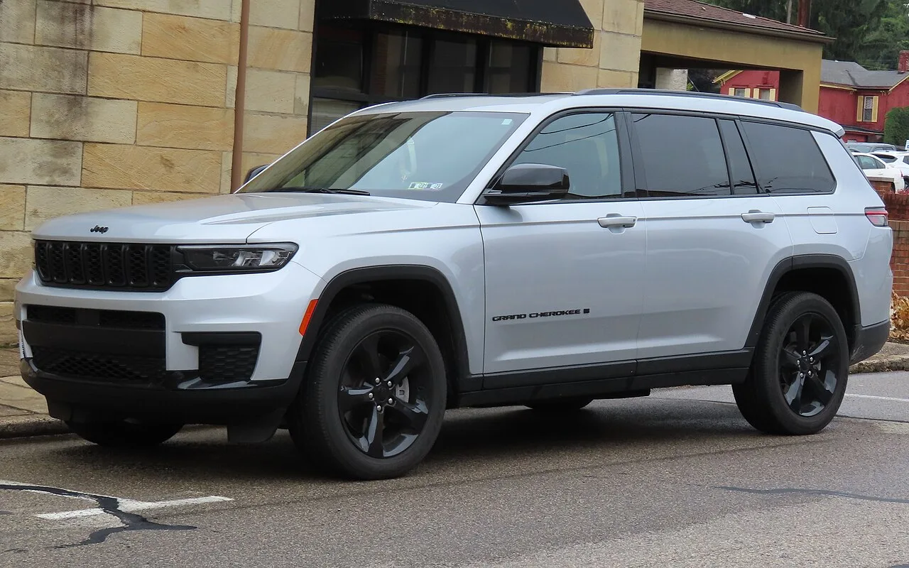은색 지프 그랜드 체로키 L의 전면 및 측면 모습, 블랙 그릴과 GRAND CHEROKEE L 도어 레터링이 보인다