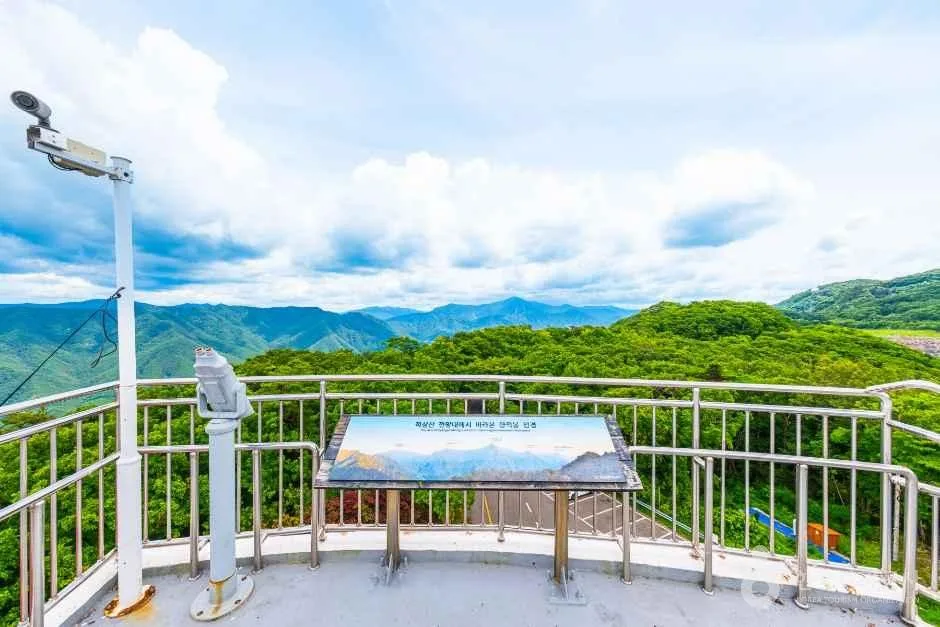 전망 데크 난간 옆에 안내판과 망원경이 놓이고 먼 산이 보이는 모습