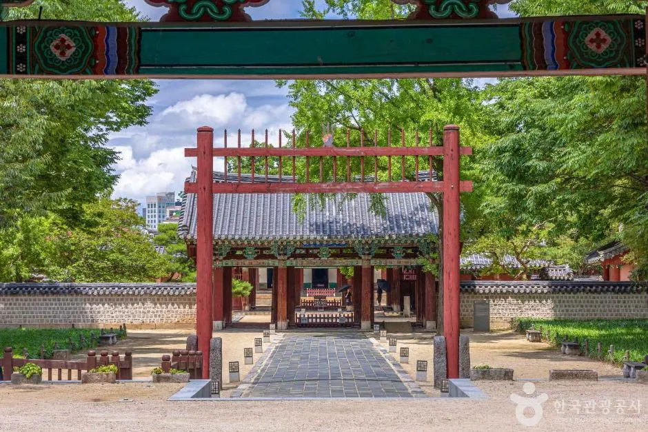푸른 나무 사이로 붉은 홍살문과 그 너머 전각으로 이어지는 진입로가 보이는 경기전 입구