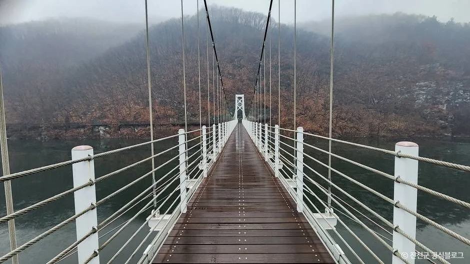 안개 낀 호수 위로 흰 난간의 보행 다리가 길게 이어진 모습