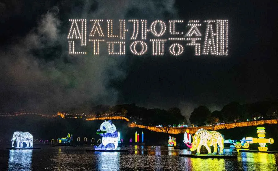 밤하늘에 드론이 만든 '진주남강유등축제' 글자 조명이 떠 있고 그 아래 코끼리, 판다, 코뿔소 등 동물 모양 대형 유등이 남강 위에 떠 있다