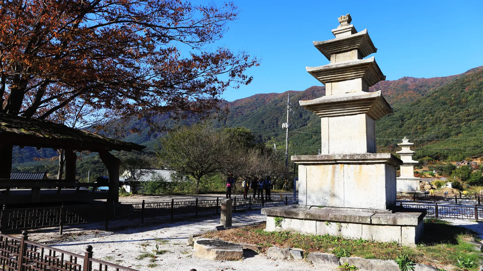 단속사지 삼층석탑과 그 앞을 지나는 둘레길 도보 여행자들, 뒤로 산청 능선이 보인다