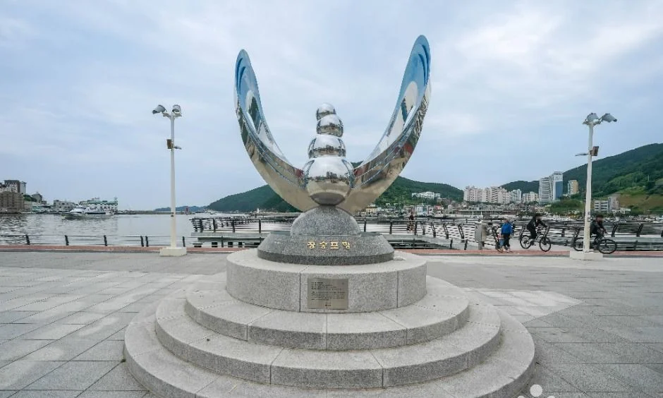 은색 조형물이 서 있는 장승포항 광장과 바다