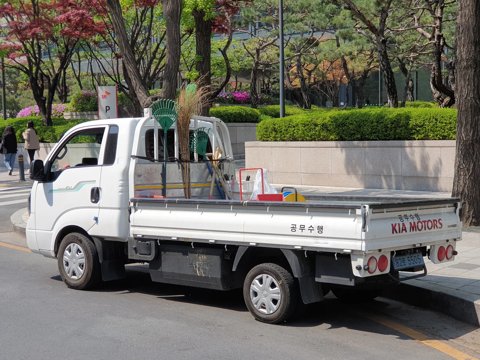 기아 봉고3 EV 후면 우측 45도, 적재함에 원예 도구를 실은 흰색 픽업 트럭, 후면에 KIA MOTORS 레터링