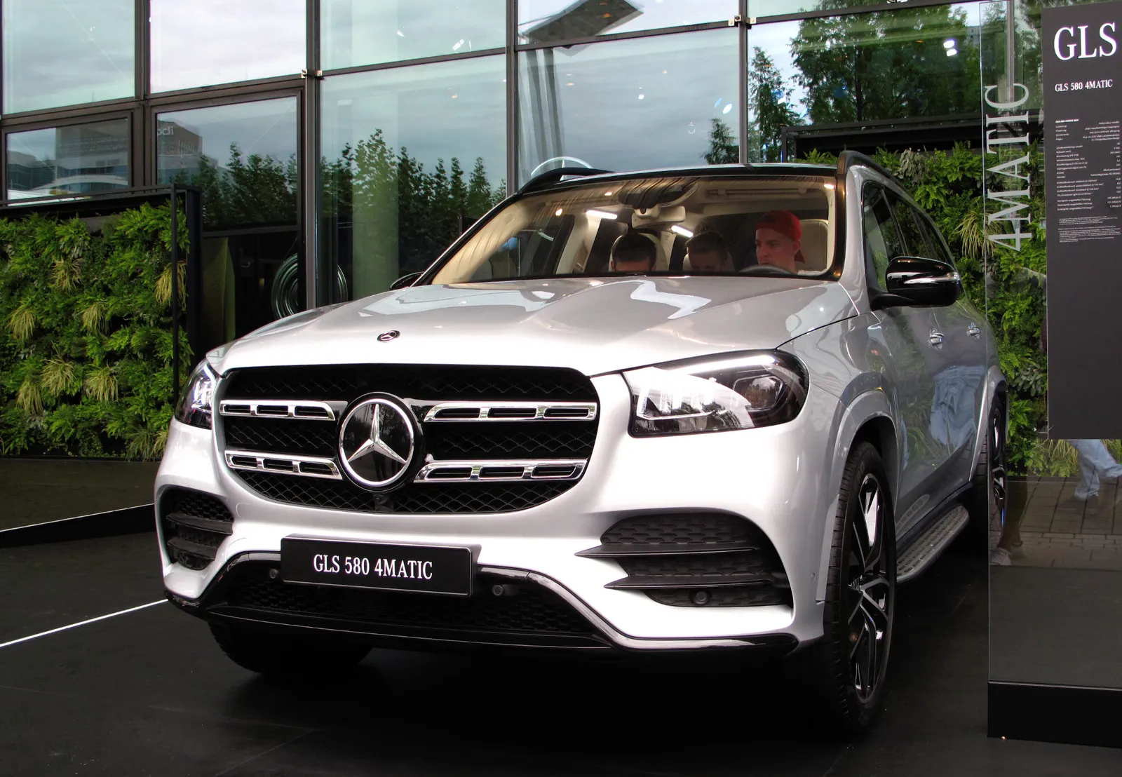 모터쇼 전시장에 세워진 은색 메르세데스-벤츠 GLS 580 4MATIC의 전면 모습, 크롬 그릴과 GLS 580 4MATIC 배지가 보인다