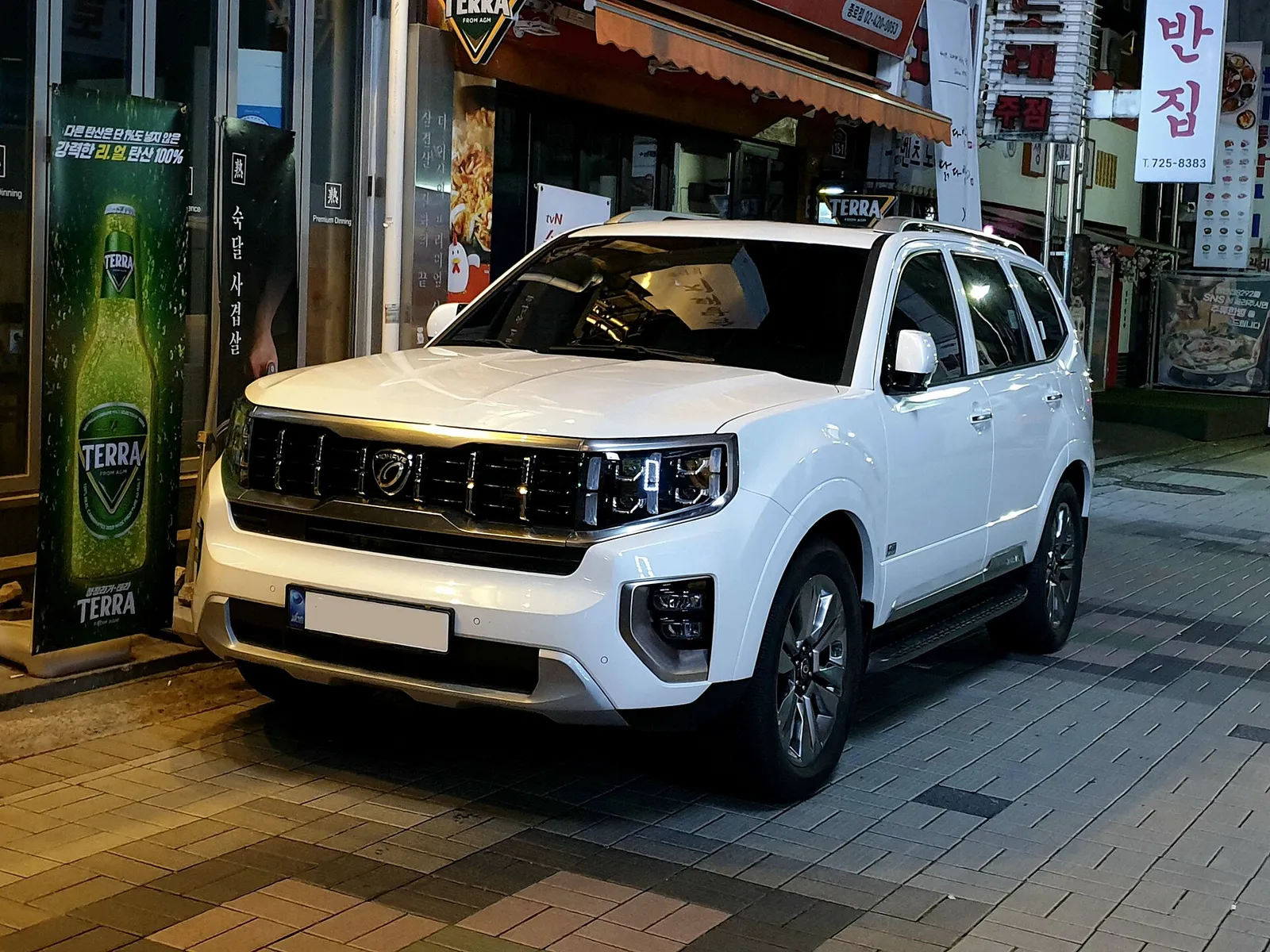 흰색 기아 모하비 전면, 세로형 그릴과 헤드램프가 보이는 도심 골목 주차 모습