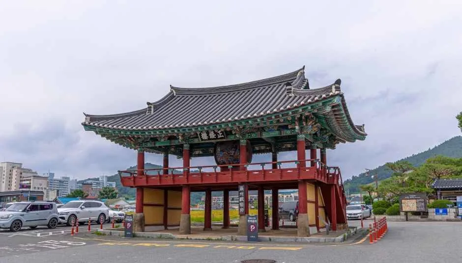 붉은 기둥과 녹색 단청의 2층 누각 정수루, 앞쪽으로 도로와 차량이 보인다